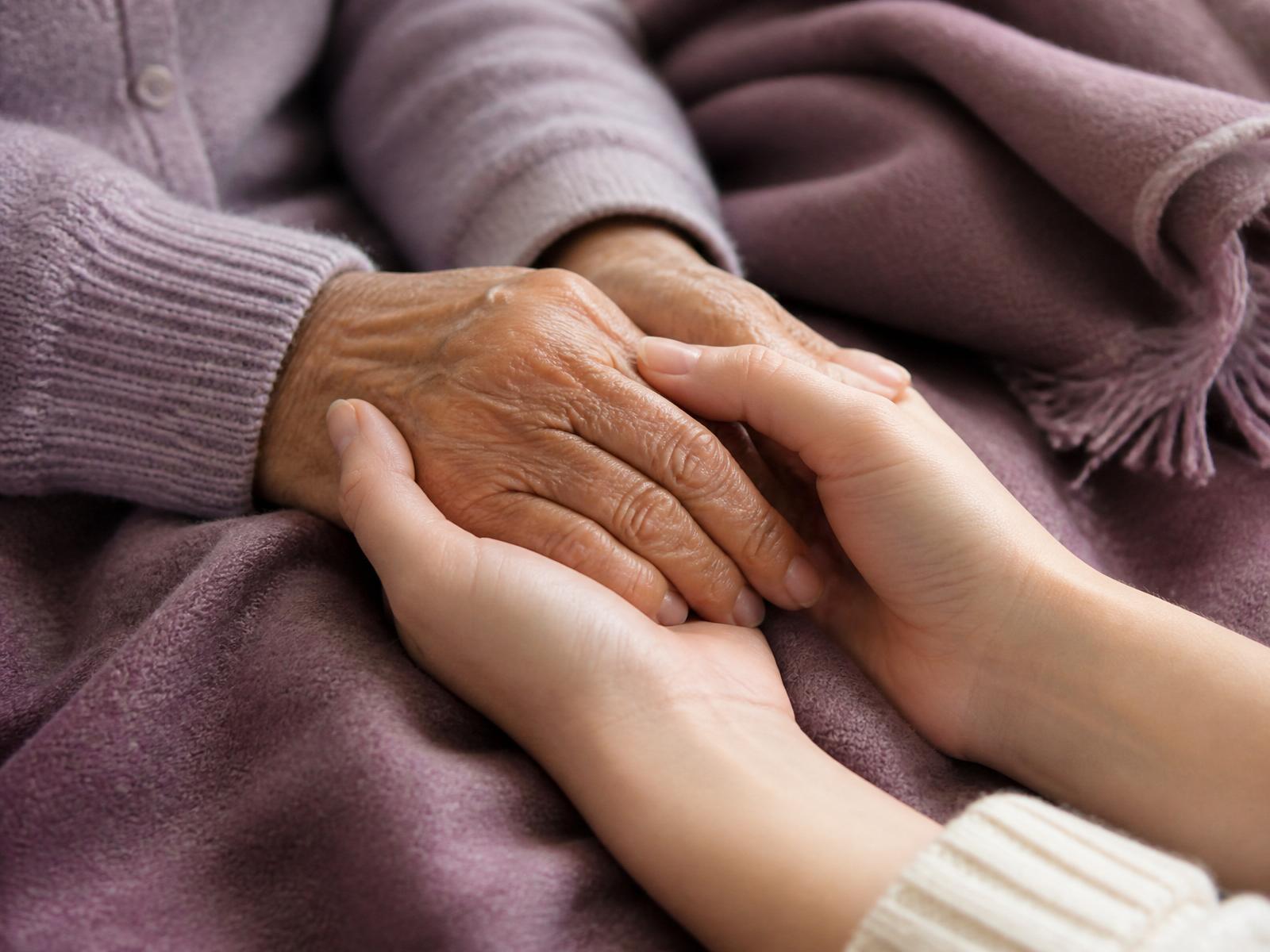 A geriatric care manager gently holding an older client's hand — compassionate care coordination
